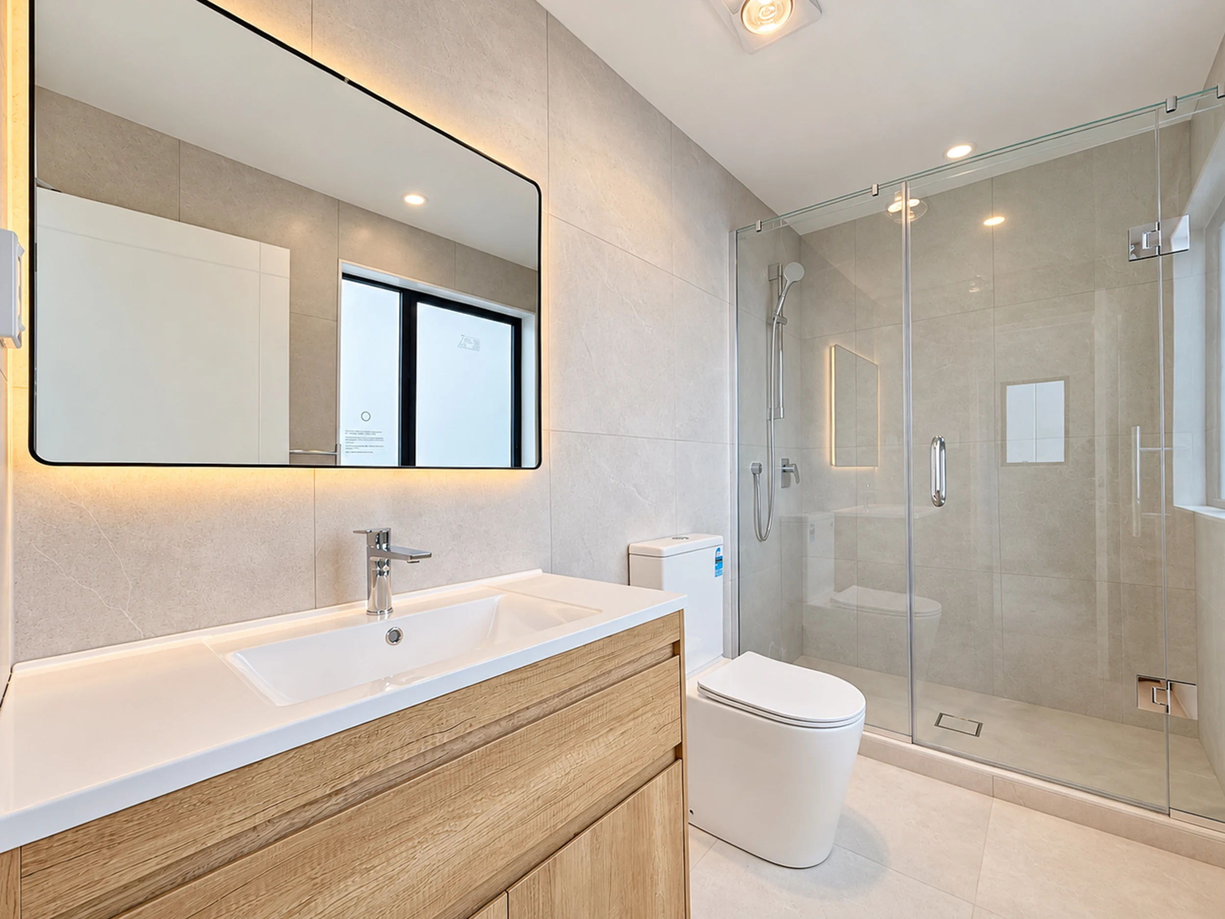 Bathroom with a wide vanity, illuminated mirror and glass shower